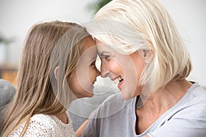 Happy middle-aged grandma and little granddaughter touching nose