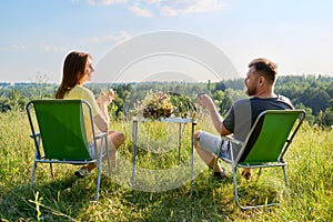 Happy middle-aged married couple having rest outdoors, in meadow, back view.