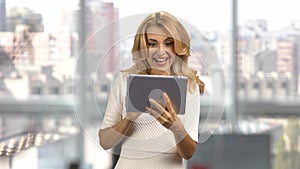 Happy middle aged mature caucasian blonde lady holding digital tablet indoors.