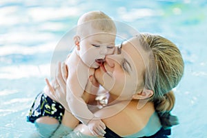 Happy middle-aged mother swimming with cute adorable baby in swimming pool.