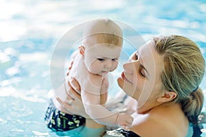 Happy middle-aged mother swimming with cute adorable baby in swimming pool.