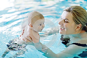 Happy middle-aged mother swimming with cute adorable baby in swimming pool.