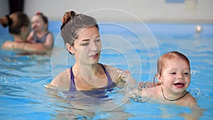 Happy middle-aged mother swimming with cute adorable baby in swimming pool. Smiling mom and little child, newborn girl