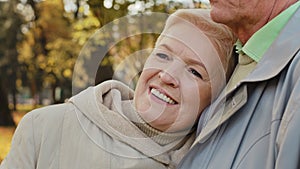 Happy middle aged pretty caucasian elderly woman grandma smiling stand relax in autumn park spend time outdoors lean on