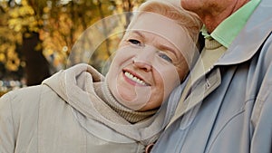 Happy middle aged pretty caucasian elderly woman grandma smiling stand relax in autumn park spend time outdoors lean on