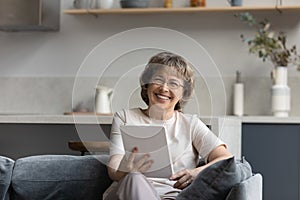 Happy middle aged retired woman with tablet looking at camera.