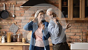 Happy middle aged spouses dancing singing in kitchen