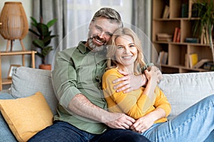 Happy Middle Aged Spouses Relaxing On Couch At Home And Hugging