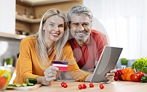 Happy middle aged spouses using digital tablet and credit card