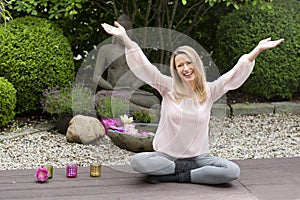 Happy middle aged woman with arms outstretched in zen garden