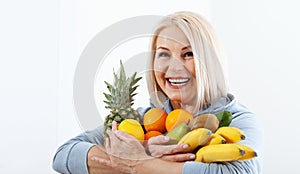 Happy middle aged woman with blond hair and beautiful smile holds products from the store in paper bag of vegetables in her hands