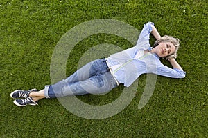 Happy middle-aged woman in casual weekend clothing relaxing on the grass in a park