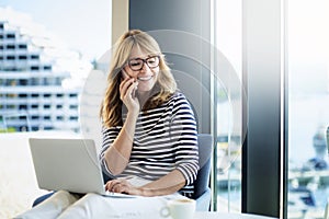 Happy middle aged woman having a call and using laptop while working from home