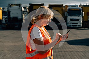 Happy middle-aged woman having a phone call in front of yellow semi-truck vehicle