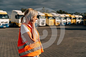 Happy middle-aged woman having a phone call in front of yellow semi-truck vehicle