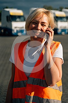 Happy middle-aged woman having a phone call in front of yellow semi-truck vehicle