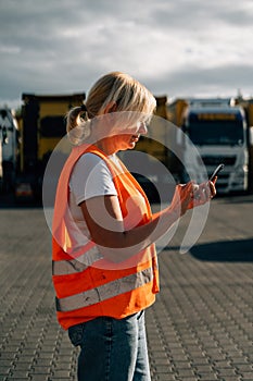 Happy middle-aged woman having a phone call in front of yellow semi-truck vehicle