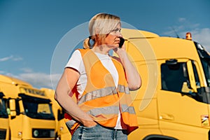 Happy middle-aged woman having a phone call in front of yellow semi-truck vehicle