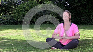 Happy middle aged woman in her forties outside cross legged practicing yoga in prayer or lotus position