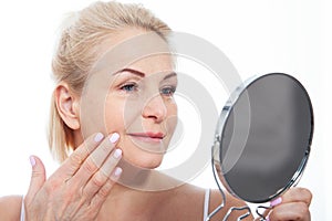 Happy middle aged woman model touching face skin looking in mirror. Smiling mature older lady enjoying healthy skin care, aging