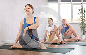 Happy middle-aged woman practicing lord of the fishes pose of yoga with her family