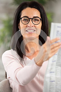 happy middle aged woman reading magazine at home