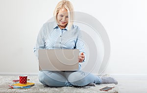 Happy middle aged woman sitting relaxed on the floor using laptop for entertainment. The concept of leisure and work