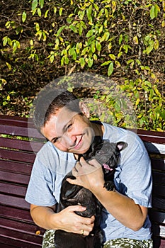 Happy middle-aged woman smiling enjoying her black pug dog on bench on parknatural background