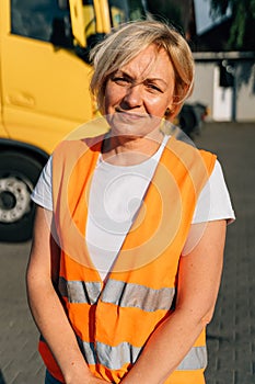 Happy middle-aged woman smiling in front of yellow semi-truck vehicle