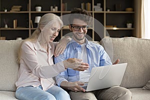 Happy middle-aged woman spend time with adult son use laptop