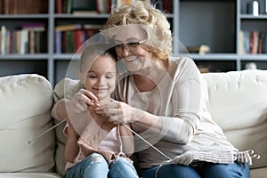 Happy middle aged woman teaching small preschool granddaughter doing needlework.