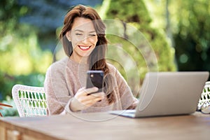 Happy middle aged woman using a smartphone and laptop while relaxing outdoor