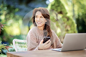 Happy middle aged woman using a smartphone and laptop while relaxing outdoor