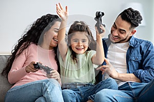 Happy middle eastern family of three playing video games together at home