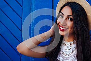 Happy middle-eastern girl smiling and looking at camera. Outdoor portrait of young woman wearing summer hat