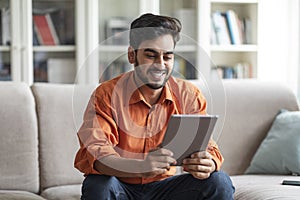 Happy middle eastern guy using digital tablet at home