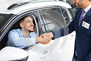 Happy middle-eastern man sitting in car shaking sales manager hand