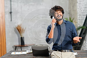 Happy middle eastern man talking on the smartphone while standing in modern loft office. Smiling successful contemporary