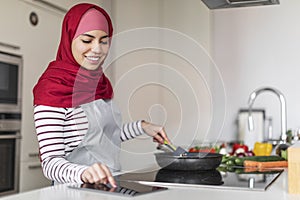 Happy middle eastern woman enjoying cooking at home, checking recipe