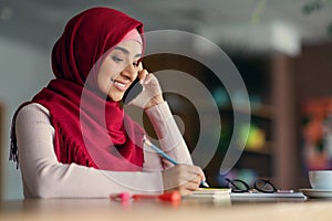 Happy middle-eastern woman in hijab having phone conversation