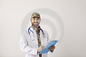 Happy military doctor in camouflage hat and medical lab coat holding clipboard and smiling