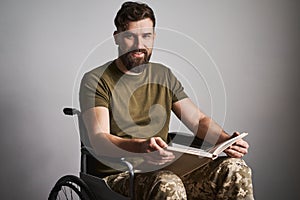 Happy military man sitting in a wheelchair and watching album photos