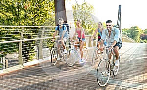 Happy millenial friends having fun riding bike at city park - Friendship concept with young millennial students biking together