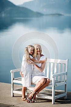 Happy millenial mother and blonde teenager daughter in white family look dresses walking by the harbor and seashore  in a