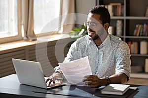 Happy millennial african american businessman in eyewear doing paperwork. photo