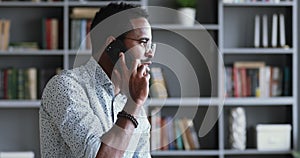 Happy millennial african american businessman talking on phone in office