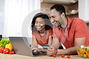 Happy millennial african american couple in same t-shirts look at laptop, use credit card