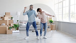 Happy millennial african american husband and wife dancing in new apartment, celebrating buying flat