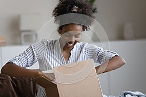 Happy millennial african american woman unpacking parcel.