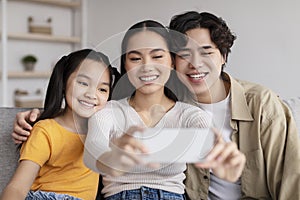 Happy millennial attractive japanese man, woman and teenager girl making photo together on smartphone